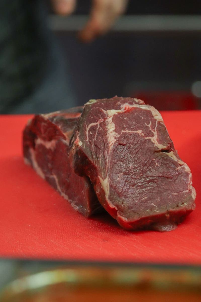 A thick cut of raw beef on a red board