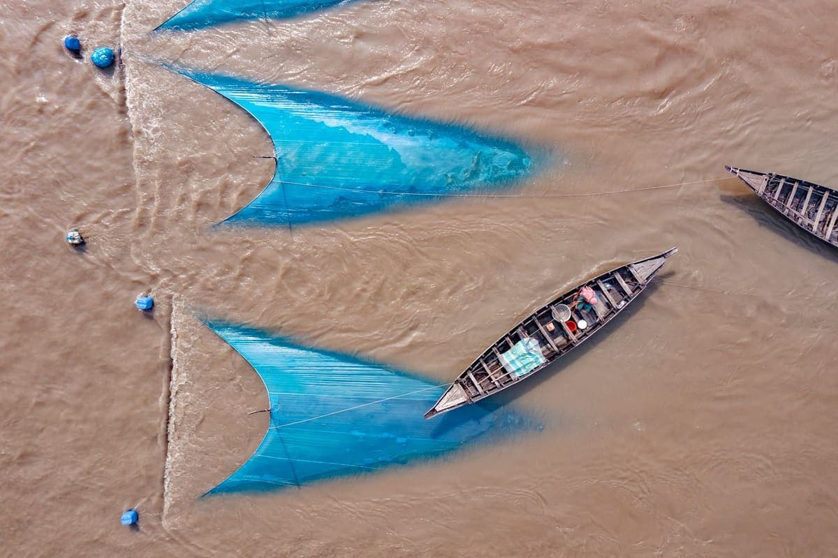 Aerial view of a fishing boat beside blue nets on a sandy river bank